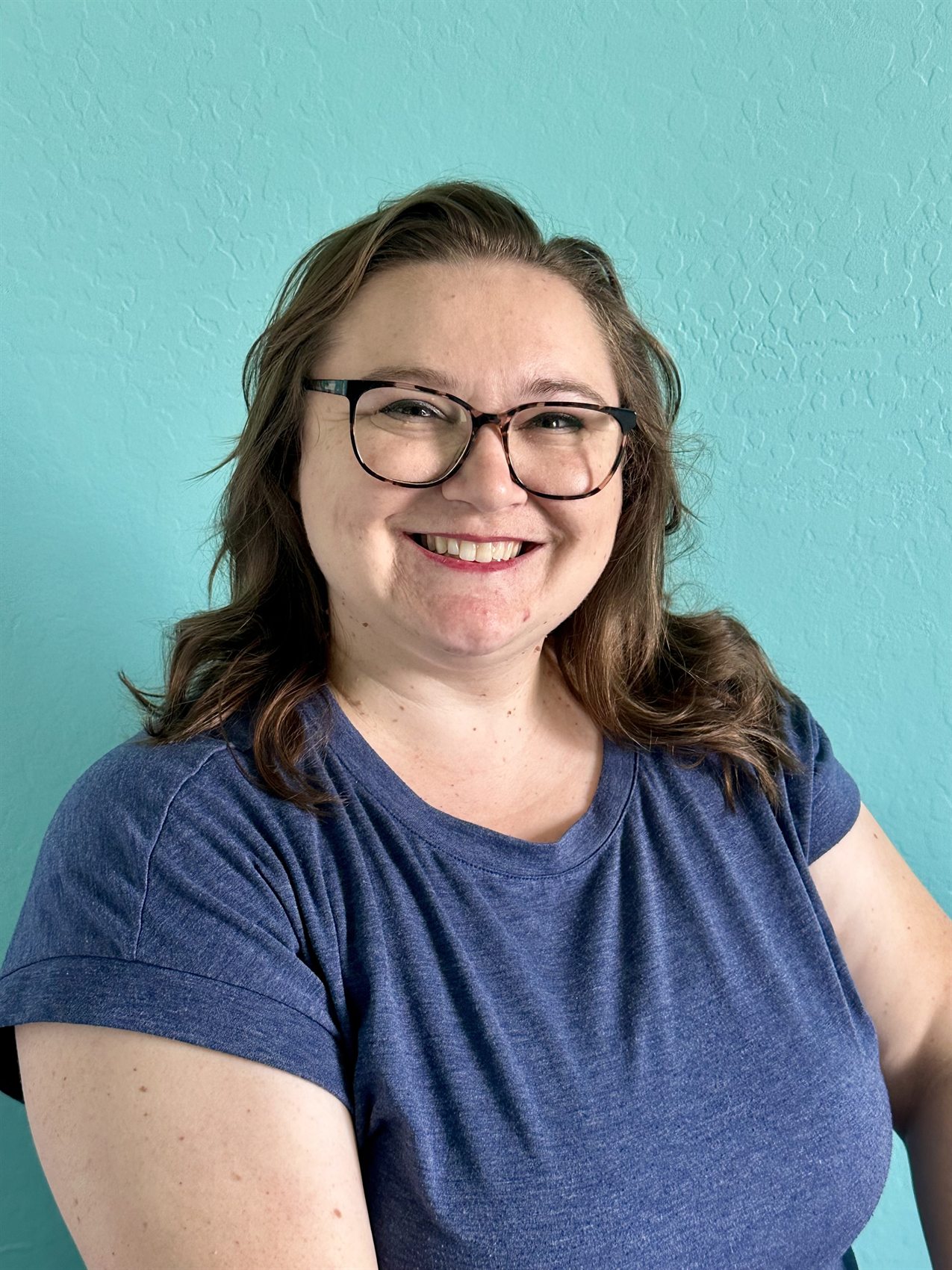 Smiling massage therapist portrait against a teal wall.